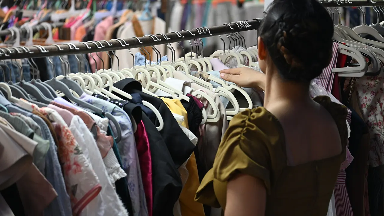 A shopper browsing a crowded rack of colourful dresses and tops in a secondhand clothing shop